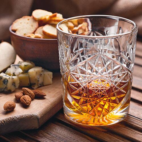 glass of spirits with nuts and cheese in background