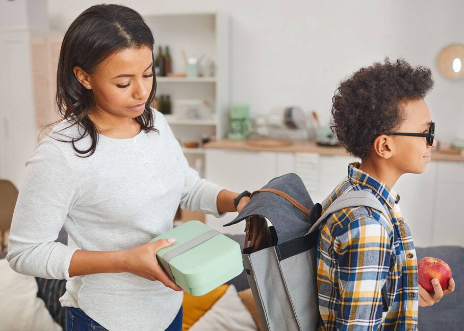 Mom putting lunch in kid's backpack