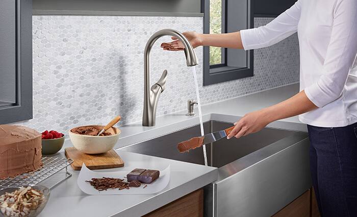 Woman washes a cake-knife over a Kohler stainless-steel, farmhouse-style sink.