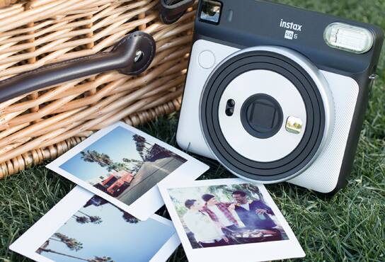 A polaroid camera sits nearby a picnic blanket and printed family photos.