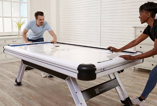 Two people play air hockey in a recreation room.