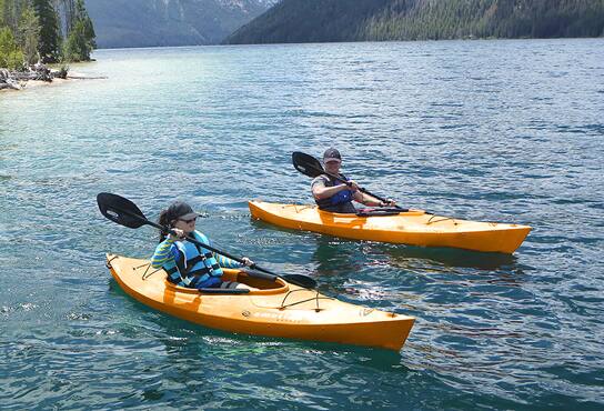 Two kayakers paddle across a lake.