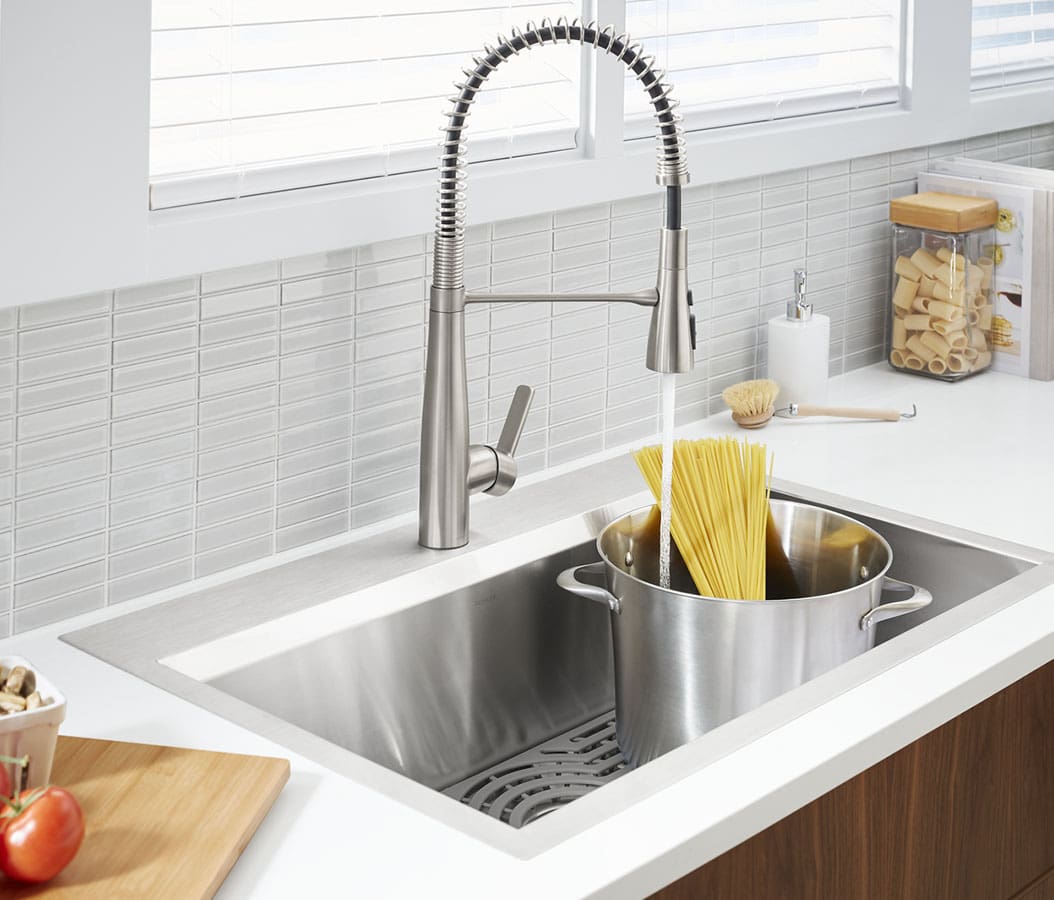 Natural, bright light illuminates bathroom adorned with white porcelain subway tiles on the back wall and light-brown hardwood flooring. A gleaming Kohler porcelain white toilet, porcelain white pedastal sink with nickle-plated faucet fixtures provide the main focus.