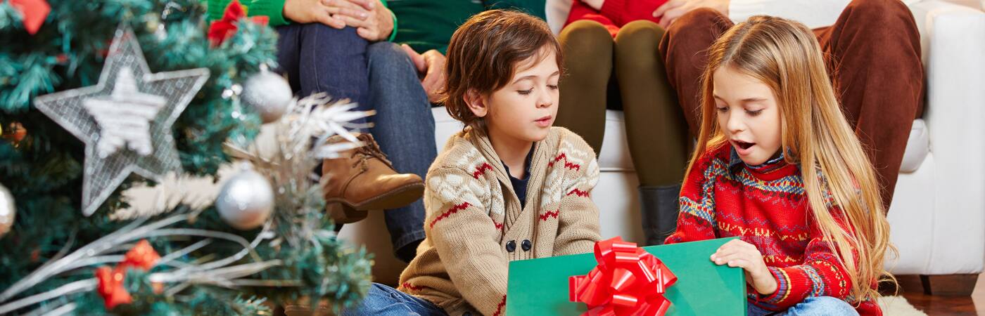 Two children unwrap a Christmas present with a big bow on top.